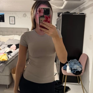 Beige slim t-shirt  - Snygg beige t-shirt med rund hals och korta ärmar. Modellen är slim och sitter tight mot kroppen, perfekt för en clean och enkel look. Materialet känns mjukt och stretchigt, vilket gör den skön att bära hela dagen.