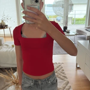 Röd croppad topp med fyrkantig ringning - Snygg röd croppad topp med korta ärmar och fyrkantig ringning. Toppens tighta passform framhäver figuren och den är perfekt att matcha med jeans eller kjol. Enkel och stilren design som ger en trendig vibe.
