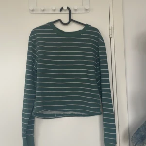 Grön randig långärmad tröja - Säljer en grön långärmad tröja med vita horisontella ränder. Tröjan har en avslappnad passform och är något croppad i modellen. Perfekt för dig som gillar en enkel men snygg stil. Passar till både jeans och kjol.