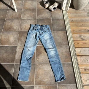 Replay Anbass ljusblå jeans, stl 29 - Säljer ett par Replay Anbass jeans i ljusblå tvätt med snygga slitningar och klassisk femficksdesign. Jeansen har smal passform och raka ben, perfekt för dig som gillar en modern och avslappnad stil. Materialet är mjukt jeans och midjan är normal.