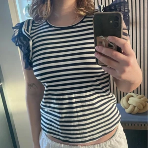 Randig topp med volangärmar - Säljer en svartvit randig topp med transparenta volangärmar i mörkblått. Toppen är köpt i Italien så har ingen aning om märke. Använd en gång🤍