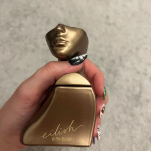 Eilish parfym av Billie Eilish - Unik parfymflaska i form av en bronsfärgad byst från Billie Eilish. Flaskan har en matt metallisk finish och är designad som en stiliserad överkropp. Perfekt för dig som gillar snygg och annorlunda design på parfymflaskor.