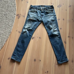 Blåa jeans från Replay Anbass - Säljer ett par blåa Replay Anbass jeans med slitningar och hål på låren och knäna. Jeansen har en slim passform och klassisk femficksdesign. Materialet är jeans i bomull och de har en snygg tvättad look med ljusare partier. Priset är inte hugget i sten