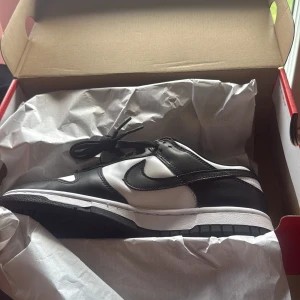 Nike Dunk Low( pandor) - Nike Dunk Low i svart och vitt med klassisk Swoosh-logga på sidan. Skon har snörning, platt sula och rund tå. Tillverkad i skinn och syntetmaterial, perfekt för dig som gillar stilrena sneakers med retrovibbar. Finns i alla sizes skriv gärna om du är intresserad av att köpa,(oanvända), (kvitto finns), intressekoll