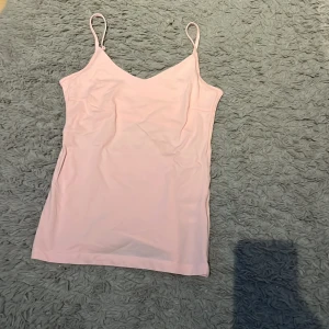 Ljusrosa linnetopp med smala axelband - Säljer en ljusrosa linnetopp med smala axelband och v-ringad hals. Toppen är enkel och stilren, perfekt att matcha med jeans eller kjol. Materialet känns mjukt och stretchigt, vilket gör den bekväm att bära hela dagen.