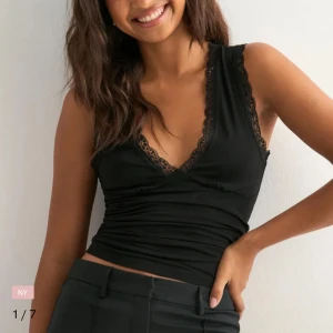 Svart ärmlös linnetopp med spets - Supersnygg svart linnetopp med djup v-ringning och spetsdetaljer längs kanterna. Toppen är figurnära och croppad, perfekt att styla med höga byxor. Mjuk och stretchig känsla, passar dig som gillar en clean men ändå feminin look. Helt ny, tog bara bort lappen tyvärr.