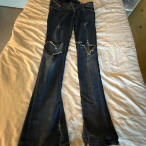 Mörkblå bootcut jeans med slitningar - Säljer ett par mörkblå bootcut jeans med slitna detaljer och hål på knäna. Jeansen har råa, fransiga benslut med slits och klassiska fem fickor. Perfekta för dig som gillar en edgy och avslappnad stil. sydde själv dem till bootcut, är i bra skick och jag använde dem i vintras sitter super fint och är väldigt lågmidjad, köpt på plick och det är disel jeans, storlek w27 L34, passar mig som är 176💕