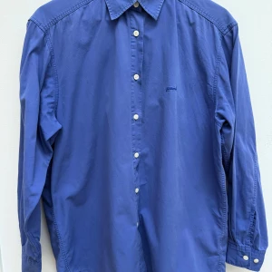 Blå Peak Performance skjorta  - Säljer en blå oversized skjorta från Peak Performance i storlek XL. Skjortan har klassisk krage, vita knappar och lång ärm. Magisk färg, indigo-blå. Tillverkad i mjuk bomull och har diskret broderad logga på bröstet. Perfekt för dig som gillar stilren och enkel design.