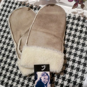 Emilia Vintervantar One Size  - Mysiga beige tumvantar från Emilia med fluffig vit insida och uppvikt kant. Tillverkade i 100% polyester, perfekta för kalla vinterdagar. Enkla och stilrena, passar dig som gillar klassisk look och vill hålla händerna varma.