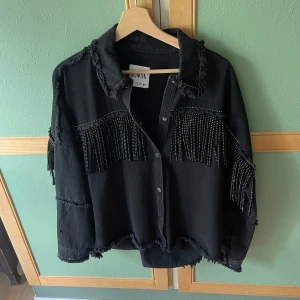 Svart jeansjacka med fransar från Zara - Cool svart jeansjacka från Zara med råa kanter och snygga fransdetaljer med nitar på bröstet och ärmarna. Jackan har knappar framtill och en oversized passform som ger en avslappnad vibe. Perfekt för dig som vill sticka ut med en edgy look. STL S, mycket fint skick!🩶🫶🏼