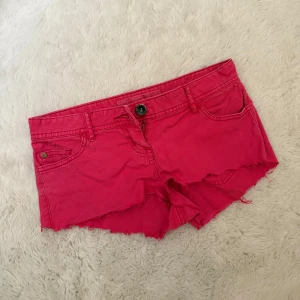 Skrikrosa Lågmidjade Jeansshorts  - Hej! Säljer dessa skitsnygga skrikrosa lågmidjade jeansshortsen med slitningar då dom tyvärr inte kommer till användning. Jeansshortsen är köpta second hand men är i mycket fint skick och har inga defekter. På ena bakfickan på shortsen finns det ett ”D” som ger en snygg detalj! Om du skulle fundera över något är det bara att höra av dig annars går det superbra att trycka på ”köp”.