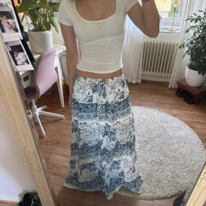 Blåvit långkjol med blommigt mönster - Superfin långkjol i vitt och blått med blommigt mönster, har resår, fint skick! Köpt secondhand men ska vara köpt utomlands sedan innan🫶 pris går att diskutera!!