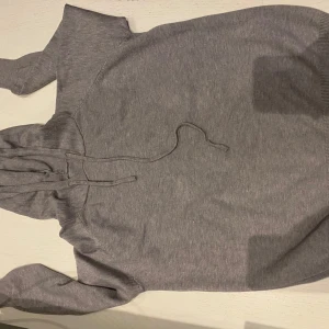 Grå hoodie med huva och snörning - Säljer en enkel grå hoodie med huva och snörning framtill. Tröjan har långa ärmar och är tillverkad i mjukt bomullsmaterial, perfekt för chill dagar. Klassisk passform och stilren look som funkar till jeans eller mjukisbyxor.