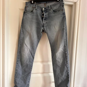 Ljusblå Levi's 501 jeans - Klassiska ljusblå Levi's 501 jeans med raka ben och knappgylf. Jeansen har fem fickor och tydliga sömmar, samt den ikoniska läderpatchen bak i midjan. Perfekta för en avslappnad stil.