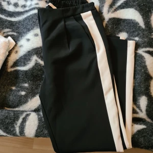 Svarta stretchiga & stiliga byxor  - Svarta byxor med vit rand längs sidorna. Byxorna har resår i midjan och fickor fram. Av märket Pieces.