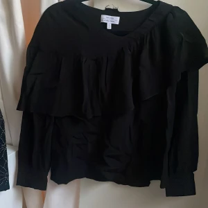 Svart volangblus från & Other Stories -  En svart blus från & Other Stories Paris Atelier med volangdetaljer framtill och långa ärmar. 