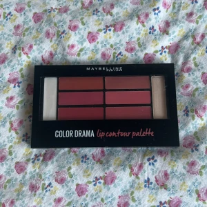 Maybelline Color Drama Lip Contour Palette - En läpp-palett från Maybelline med sex olika nyanser i rosa, nude och rödtoner, samt en primer och en highlighter. Paletten innehåller både matta och skimrande färger och kommer med en liten sminkborste. Perfekt för att skapa olika läpp-looker. Helt oanvänd och som ni kan se är borsten i sin plastförpackning och helt oanvänd också. Kommer med steg på hur man kan sminka sig med produkten. 