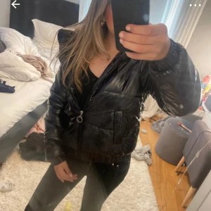 Svart glansig pufferjacka med dragkedja - Säljer en svart glansig pufferjacka med dragkedja och huva. Jackan har långa ärmar, resår vid ärmslut och midja samt stora fickor framtill. Perfekt för kyligare dagar och riktigt snygg till vardagslooken. Bilderna är från min vinted därför ❤️