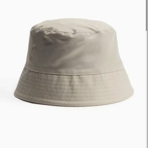 Beige och vit bucket hat - Två stilrena bucket hats i beige och vitt. Klassisk form med rundad kulle och nedåtlutande brätte. Perfekt accessoar för sommaren och enkel att matcha med olika outfits.