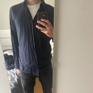 Mörkblå skjorta med klassisk krage - Säljer en stilren mörkblå skjorta med klassisk krage och knäppning framtill. Skjortan har långa ärmar och är perfekt för dig som gillar en enkel och tidlös look. Passar till många olika outfits och är lätt att matcha.