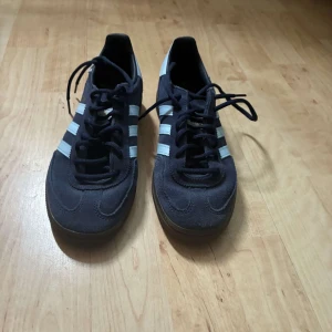 Adidas Spezial sneakers i svart mocka - Säljer ett par Adidas Spezial sneakers i svart mocka med vita ränder och gummisula. Klassisk design med snörning och guldfärgad Spezial-text på sidan. Perfekta för dig som gillar retrostil och streetwear.