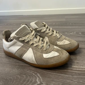 Beige och vita sneakers med gummisula - Säljer ett par klassiska sneakers i beige mocka och vitt skinn med bruna gummisulor. Skorna har snörning och en stilren design som passar till mycket. Perfekta för dig som gillar en clean och tidlös look. Inga box