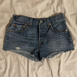 Levi's 501 jeansshorts med fransig kant - Supersnygga och trendiga  blå jeansshorts från Levi's 501 med fransig kant och femficksmodell. Shorts med lågmidja och slitna detaljer framtill. Perfekta för sommaren💞💞 passar XXS/XS eller W24 pris kan diskuteras 🩷