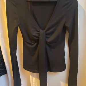 Svart långärmad omlottopp från Gina Tricot -  långärmad topp från Gina Tricot med djup v-ringning och knyt framtill.