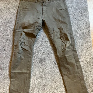Beiga chinos från Dr Denim - Säljer ett par klassiska beiga chinos från Dr Denim. Byxorna har normal passform, snedställda fickor fram och stängs med knapp och dragkedja. Perfekta till vardags och lätta att matcha med olika stilar.