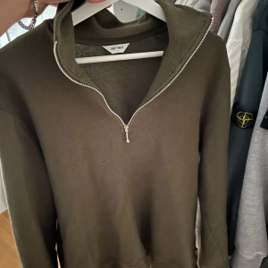 Halv zip Olivgrön tröja/ East West  - Säljer en olivgrön tröja från East West med halv dragkedja framtill och hög krage. Tröjan har lång ärm och är tillverkad i ett mjukt, stickat material. Perfekt för lager-på-lager och enkel att matcha med jeans eller byxor.