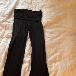 Svarta byxor från Gina Tricot - Svarta byxor från Gina Tricot med bred midja och utsvängda ben. Byxorna är mjuka och har en enkel, stilren design som passar till många olika outfits. Perfekta för dig som gillar bekväma och snygga byxor.