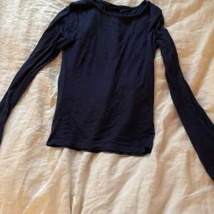 Mörkblå långärmad topp från Gina Tricot - En enkel och stilren mörkblå långärmad topp från Gina Tricot. Modellen har rund halsringning och är tillverkad i mjuk bomull. Perfekt att styla till jeans eller kjol för en clean look.