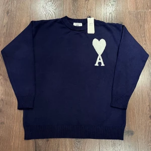Mörkblå AMI Paris tröja/sweatshirt med vit logga - Super bekväm och snygg tröja från AMI Paris. Tröjan är aldrig använd och är helt ny. Lappen sitter kvar på tröjan fortfarande. Tröjan är i storlek L. Tröjan har ett super bekväm och smidig material. Tveka inte på att ställa frågor.