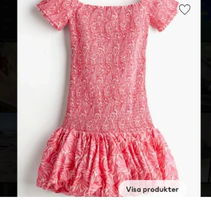 Rosa offshoulder klänning med volang - Söt rosa kortklänning med vitt mönster och offshoulder-design. Klänningen har smockad överdel och volangig kjol. Perfekt för varma dagar och midsommarfirande.