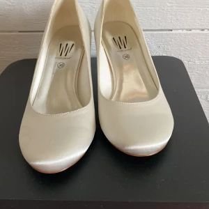 Vita pumps från Wildflower - Säljer ett par klassiska vita pumps från Wildflower i storlek 38. Skorna har rund tå, låg klack och är tillverkade i ett glansigt material som ger en elegant look. Perfekta för bal eller festliga tillfällen.