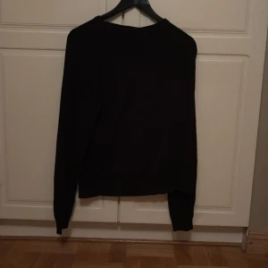 Svart stickad tröja från Cottonfield - En klassisk svart stickad tröja från Cottonfield. Tröjan har rund halsringning och långa ärmar, perfekt för lager-på-lager under kyligare dagar. Enkel och stilren design som passar till det mesta.