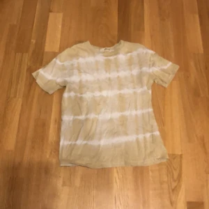 Beige och vit tie-dye t-shirt - Säljer en beige t-shirt med vitt tie-dye mönster. T-shirten har en klassisk passform och är kortärmad, perfekt för sommaren. Materialet känns mjukt och skönt mot huden.