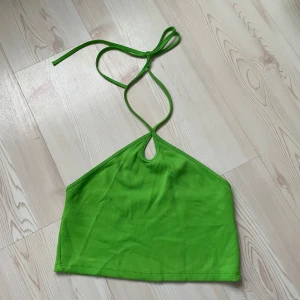 Grön ribbad halterneck-topp - Säljer en grön ribbad halterneck-topp med knyt i nacken och liten droppformad detalj framtill. Toppen är ärmlös och croppad, perfekt för varma dagar.