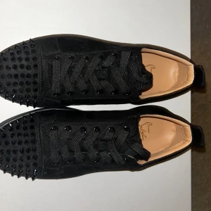 Svarta Christian Louboutin - Säljer ett par svarta sneakers från Christian Louboutin med svarta nitar på tån och klassisk röd sula. Skorna har snörning och är tillverkade i mocka med skinnfoder. Perfekta för dig som vill sticka ut med en lyxig och edgy stil. (Aldrig använda)