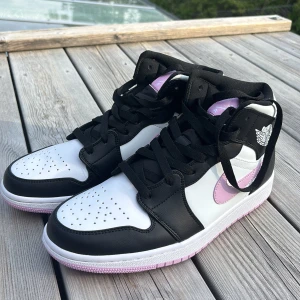 Nike Air Jordans svart/vit/rosa - Säljer ett par Nike Air Jordans med svart och vit bas samt rosa detaljer på swoosh, plös och yttersula. Klassisk high-top modell med perforerad tå och svart snörning. Skorna kommer med extra vita skosnören och StockX-tagg. Helt oanvända.