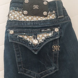 Mörk Blå Miss Me jeans med paljettdetaljer, storlek S/M  passar även dem som har M i storlek - Säljer ett par mörk blå jeans från Miss Me med snygga silvriga paljettdetaljer på bakfickorna och dekorativa knappar. Jeansen har broderad logga och kontrastsömmar som ger en unik look. Kunde tyvärr inte behålla pågående av att de passar inte mig😓