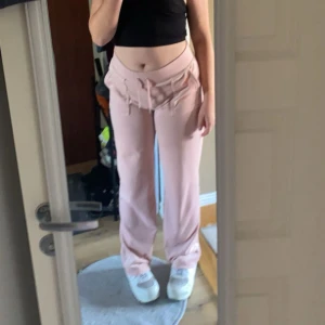 Ljusrosa Juicy Couture Byxor - Säljer ett par ljusrosa mjukisbyxor från Juicy Couture med dragsko i midjan och raka ben. Byxorna har en avslappnad passform och är perfekta för en chill stil. Mjukt material och bekväma att bära hela dagen.