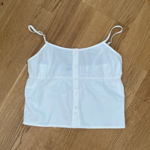 Vit linnetopp från Brandy Melville - Linne från Brandy Melville med smala axelband och knappar framtill. Perfekt för varma dagar och enkel att matcha med olika outfits.