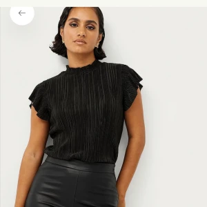 Svart plisserad blus  - Säljer en svart plisserad blus med korta volangärmar. Blusen har en lätt glansig yta som ger en elegant look. Köpt för 249kr.