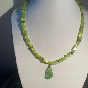 Grönt halsband med stenar och wire-wrapad hänge - Handgjort unikt halsband med ljusgröna, fyrkantiga stenar och guldfärgade detaljer. Hänget består av en grön havslipat glas insvept i guldfärgad wire. Perfekt för dig som vill sticka ut med ett färgglatt smycke.