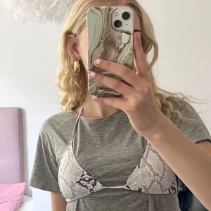 Vit bikiniöverdel med ormmönster - Trendig trekantsbikini i vitt med ormmönster. Klassisk modell med knyt i nacken och ryggen. Perfekt för sommardagar vid stranden eller poolen.