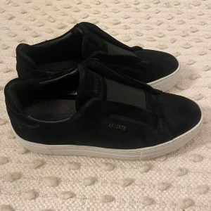 Svarta sneakers från Axel Arigato - Säljer ett par svarta sneakers från Axel Arigato med vit sula. Skorna har en minimalistisk design utan snörning och är tillverkade i mocka. Perfekta för dig som gillar stilrena och bekväma skor. Pris kan diskuteras 