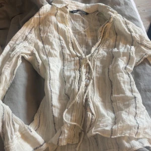 Vit randig blus från Zara - Säljer en luftig vit blus från Zara med tunna svarta ränder. Blusen har knappar framtill och knytning vid halsen. Jättebra skick och slutsåld överallt