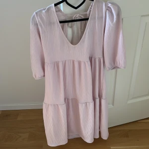 Ljusrosa klänning med puffärm och knyt i ryggen - Superfin ljusrosa kort klänning med v-ringning, puffärmar och knytband i ryggen. Storlek S