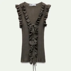 Brun ribbad topp med volang från Zara - Supersnygg brun ribbad topp från Zara med volangdetaljer längs v-ringningen och axlarna. Toppen har knyt framtill och är ärmlös, perfekt för att lyfta din outfit.